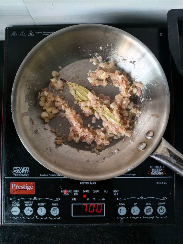 Chopped onion and garlic cooking in a pan with a bay leaf, just starting to turn translucent.