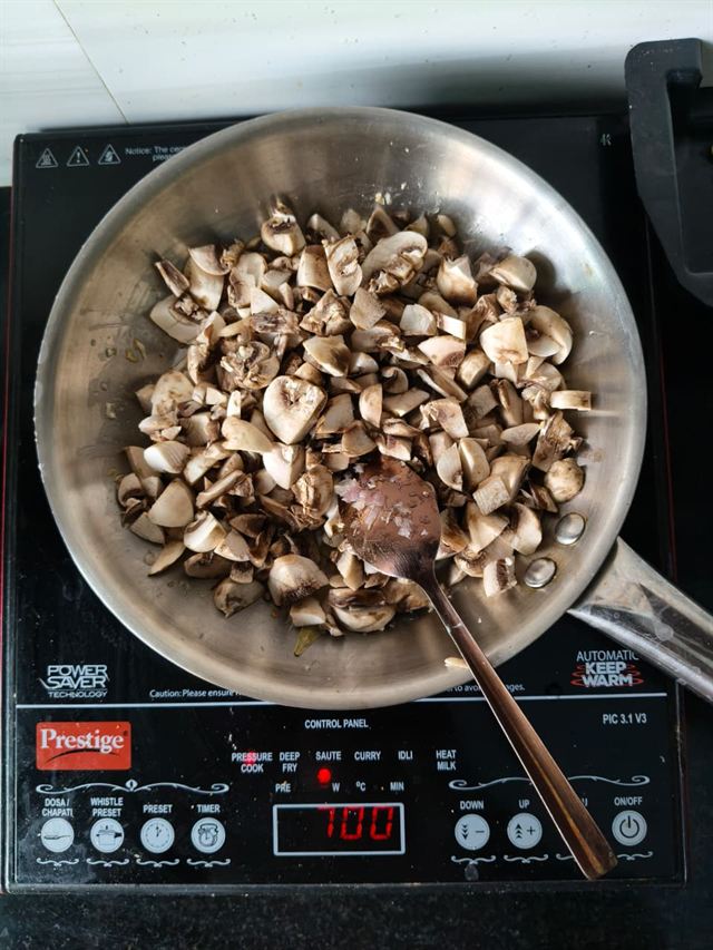 Sliced mushrooms cooking in a steel pan with a wooden spoon, releasing their liquid.