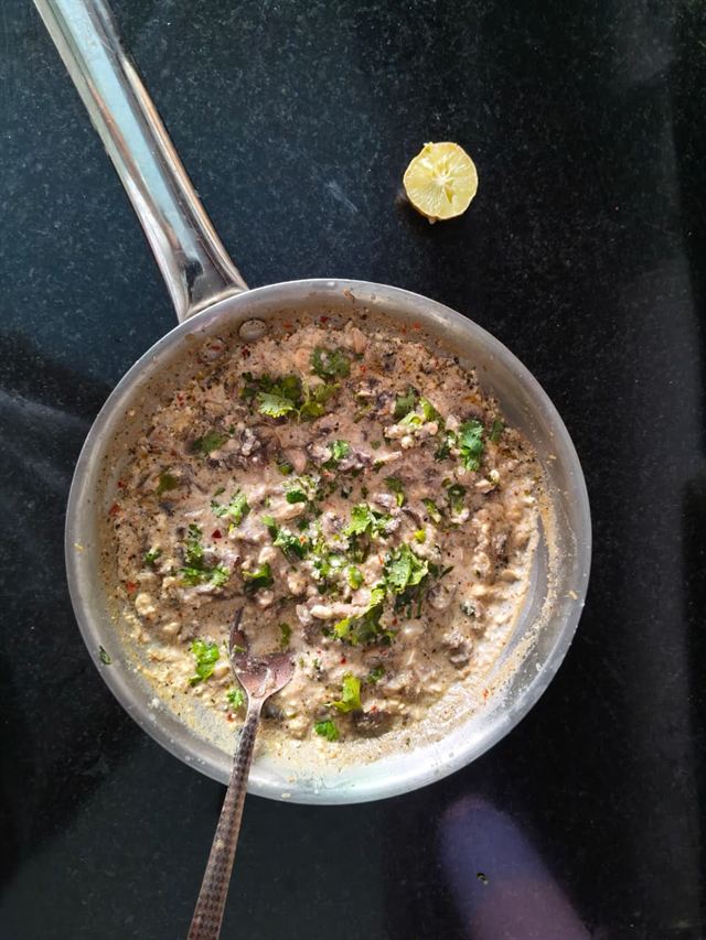 The finished mushrooms in their creamy sauce, topped with chopped coriander, a squeezed lemon half resting beside the pan.