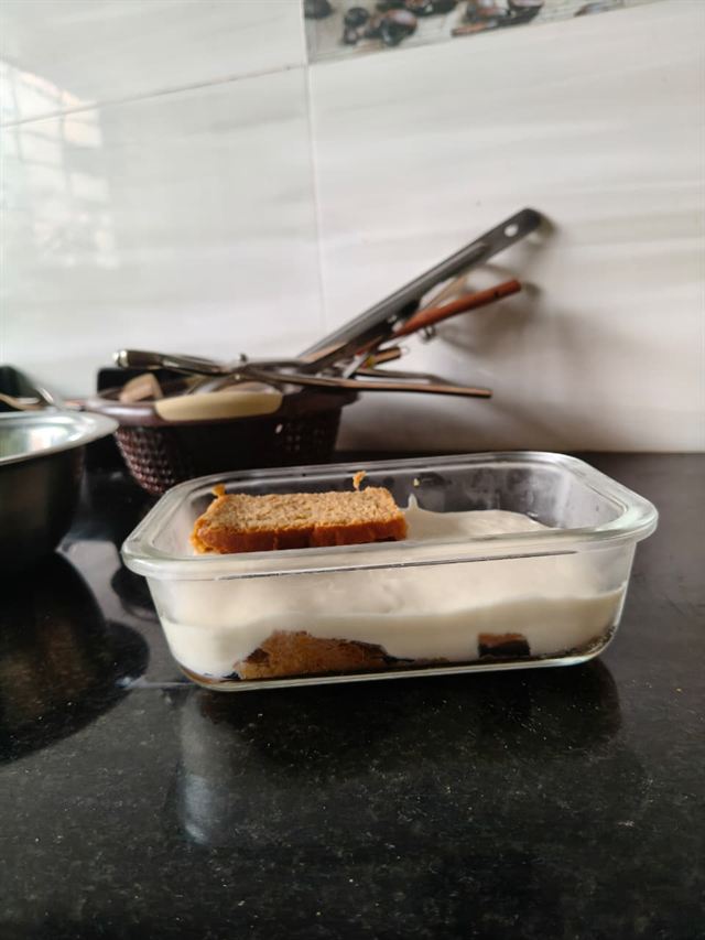 Side view of the tiramisu in progress: coffee-soaked rusk base topped with a freshly poured layer of smooth paneer cream.