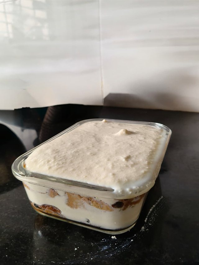 Glass dish filled with an even layer of whipped paneer cream covering the soaked rusk base, ready to chill.